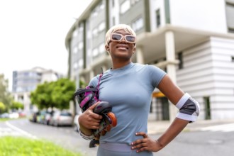 Blonde african woman posing proud holding inline skates standing in the city street