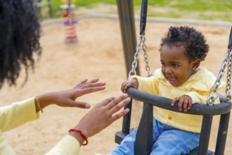 Cropped photo of an african girl and unrecognizable mother swinging in the park