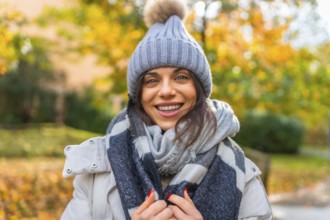 Portrait of a confident smiling woman with woolly hat and scarf in a park