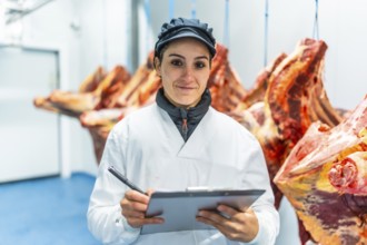 Portrait of a woman working in a meat processing factory writing notes in a clipboard