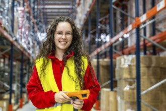 Frontal portrait of a happy young female employee holding a scanner in a distribution warehouse
