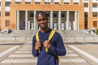 African university student holding rucksack posing at the city next to university building