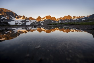 Rocky mountain peaks reflected in a small pond, mountain landscape with alpenglow at sunrise, at