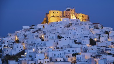 Whitewashed buildings surround an illuminated fortress under a dark blue night sky, Querini Castle,