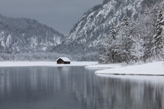 Snow covered boat shelter on Lake Almsee which is partly frozen and snow covered. Snow on the