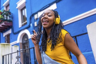 African woman singing to the camera and dancing in the street next to a blue house