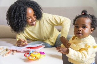 Adorable child and african mother drawing at home sitting on the sofa in the living room