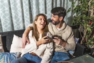 Cheerful couple enjoying a romantic evening, drinking wine and laughing together on a cozy terrace