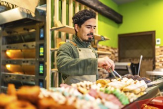 Latin young male baker arranging pastries on the counter of an artisan bakery shop