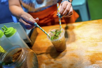 Close-up of the hands of a woman mixing mojito cocktail with straw