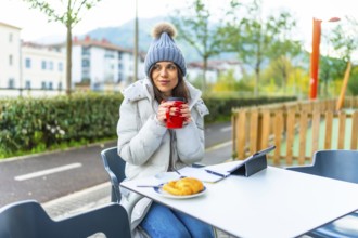 Woman enjoying cup of hot tea while using tablet in an outdoors cafeteria
