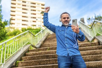 Mature man dancing while listening to music with phone in an urban stairs in the city