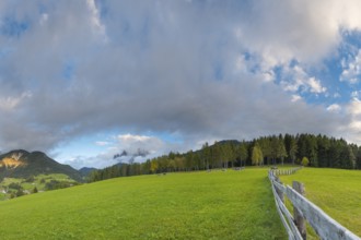 View along a wooden fence across a pasture to the mountains in the evening light, Dolomites, Odle