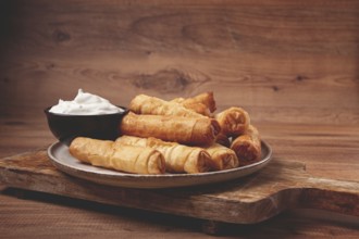 Fried spring rolls with cheese, on a wooden background, with cream sauce, no people