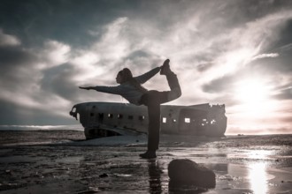 Woman on the Solheimasandur plane in Iceland performing a Natarajasana yoga pose to open the hip