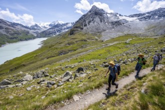 Three mountaineers on a hiking trail at a blue mountain lake, reservoir Lac des Dix, behind