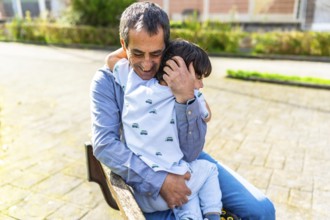 Grandfather hugging grandson while sitting on a park bench, enjoying a tender moment together