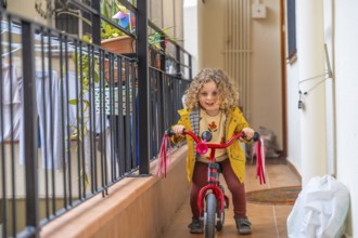 Little girl riding a pink bike in the terrace at home in a sunny day of spring