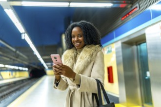 Smiling businesswoman using her mobile phone while waiting for the subway train at the station,