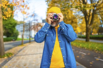 Frontal portrait of a mature modern man photographing in the city while visiting it in autumn