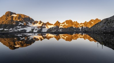 Rocky mountain peaks reflected in a small pond, mountain landscape with alpenglow at sunrise, at