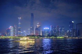 Guangzhou cityscape skyline over the Pearl River with tourist boat illuminated in the evening.