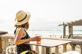 Summer vacation lifestyle. Young caucasian girl in a hat having a soda next to the beach