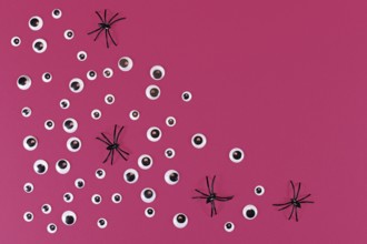 Halloween flat lay with lots of spooky googly eyes and plastic spiders on pink background with