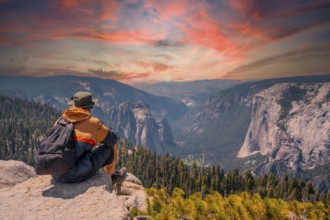 A young man on the trek sitting on the Sentinel Dome lookout in Yosemite National Park looking at