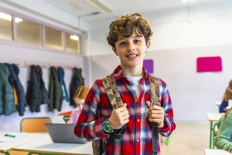 Portrait of a smiling preteen student wearing backpack in a classroom with classmates studying on