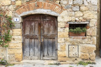 Quarry stone wall with old wooden door and house number 6, rosemary in a flower box, in the