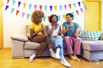 Multi-ethnic friends chatting during party at home sitting on the sofa with beers and karaoke