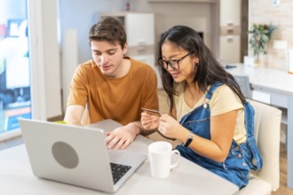Multiethnic couple using a laptop and a credit card, making online purchases together in their