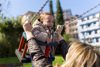 Happy little boy enjoying time on a swing while his mother lovingly pushes him in a vibrant