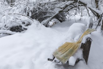 Frozen yellow towel lying on a snow covered bench in a forest near a creek