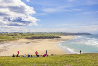 Group of hikers resting on a meadow with a scenics view at a sand beach with breaking waves and a