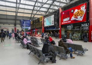 People sitting in seats in concourse area of Lime Street railway station, Liverpool, England, UK