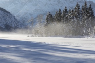 Misty morning on Lake Almsee which is frozen and snow covered. Snow on the forest with blue sky