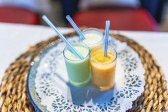 Three vibrant smoothies in glass cups with straws, placed on a decorative table setting, adding a