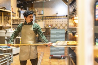Latin male baker using wooden peel to remove baked pastries from a traditional oven