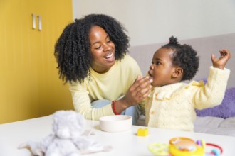 Happy african mother and cute toddler playing in the living room at home