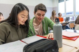 Two high school students are working together on a project in a classroom, demonstrating teamwork