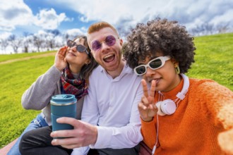 Three cheerful multi ethnic friends making funny faces and gesturing while taking a selfie with