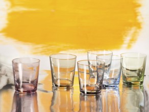 Various glasses on silver foil, yellow coloured surface behind, studio shot