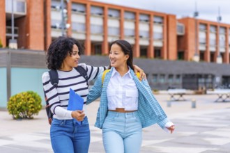 Happy multi-ethnic latin and chinese female students walking embraced along the university campus