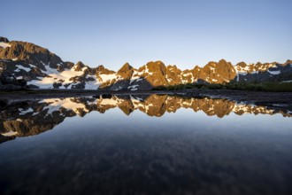 Rocky mountain peaks reflected in a small pond, mountain landscape with alpenglow at sunrise, at