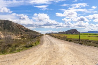 Scenic view of a gravel road stretching through the bardenas reales desert landscape under a bright