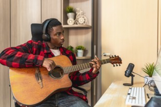 Concentrated young man playing the acoustic guitar in his home studio, composing a new song and