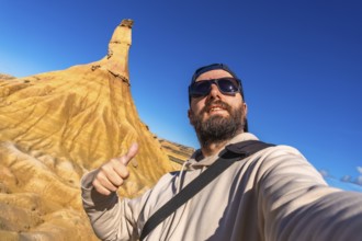 Tourist taking a selfie and gesturing thumbs up in front of a sandstone peak in bardenas reales