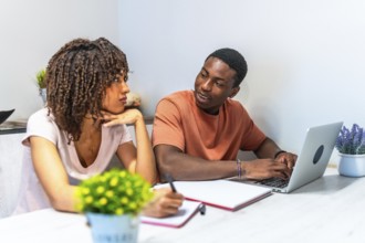 Young black couple collaborating on a laptop, taking notes and engaging in productive remote work